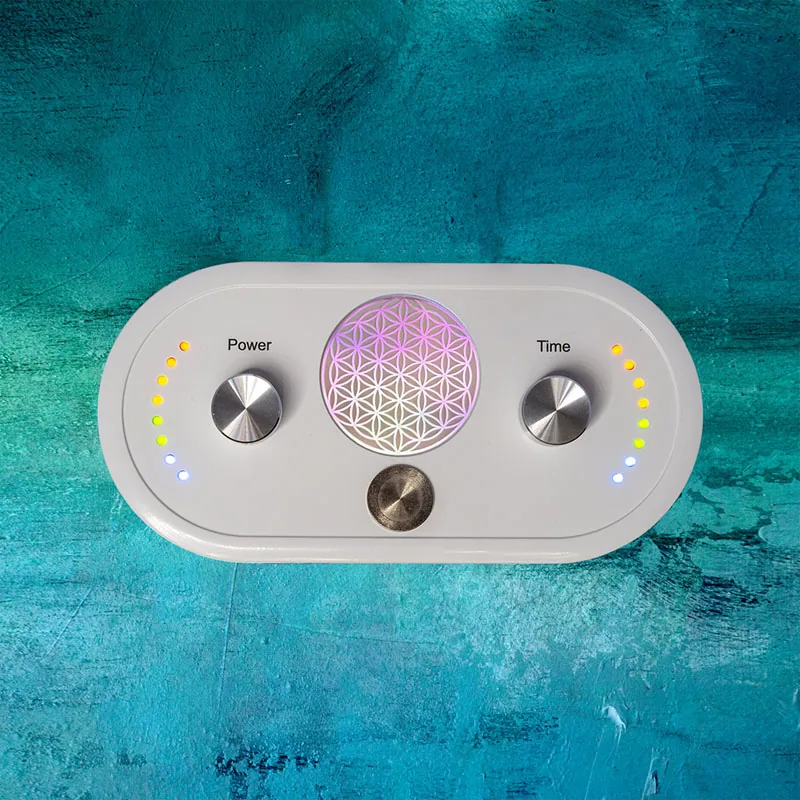 Draufsicht auf das quantumVibe-Gerät: weißes, länglich-ovales Gehäuse mit zwei silbernen Reglern, beschriftet „Power“ und „Time“, daneben je ein Bogen aus acht farbigen LEDs, in der Mitte ein schimmerndes Kreismuster aus überlappenden Kreisen und darunter ein dritter Metallknopf; Hintergrund türkisblau und strukturiert